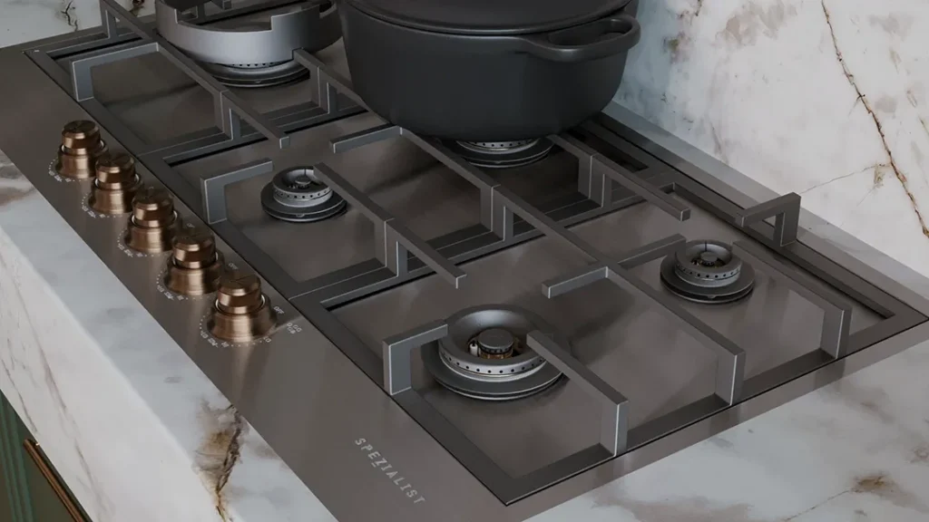 Spezialist 5 burner inset mount with stainless steel and custom cooper knobs on a light marble counter top and dark sage colour cabinetry